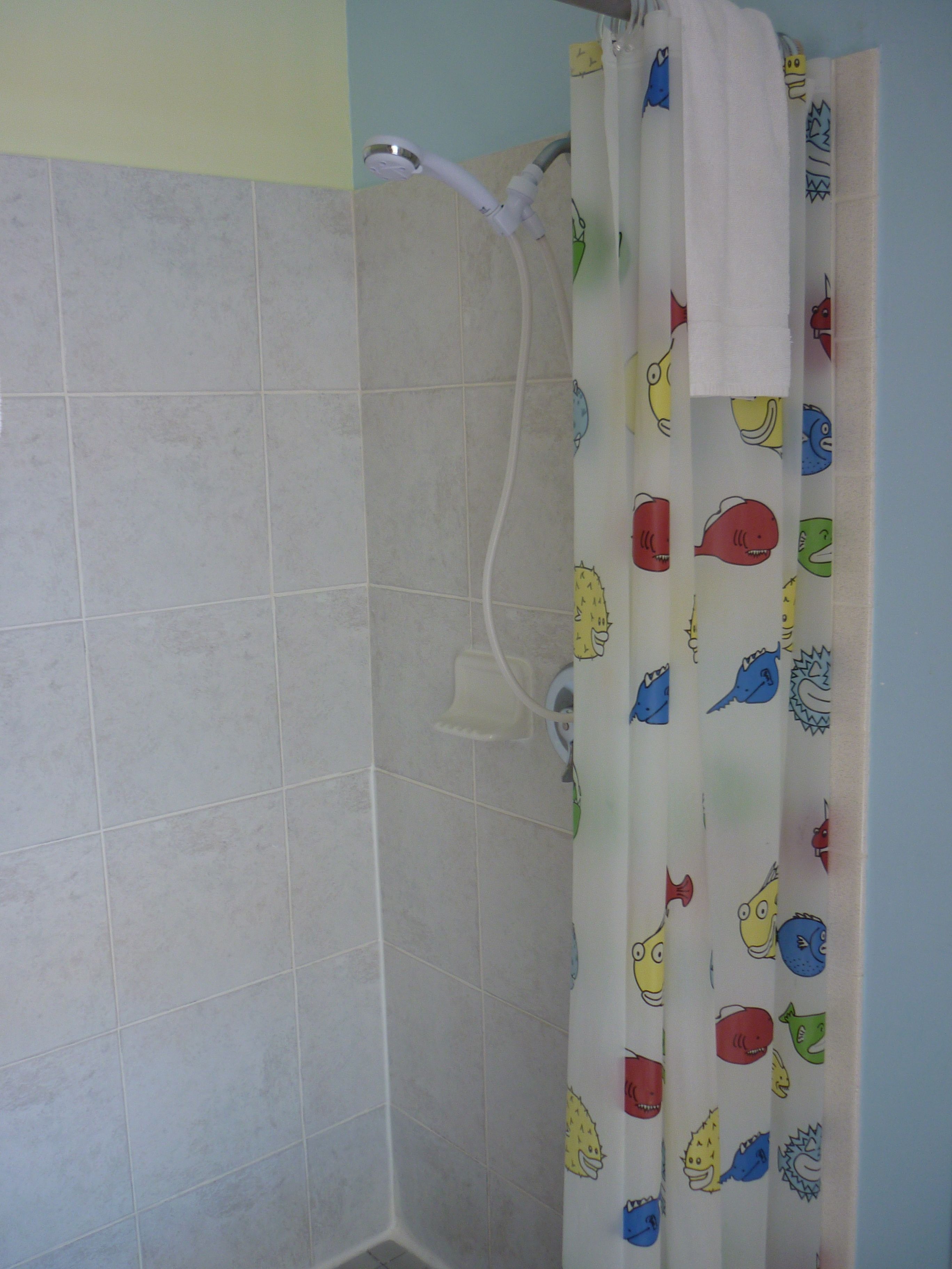 A bathroom with tiled walls, a shower curtain with cartoon fish patterns, and a visible showerhead.