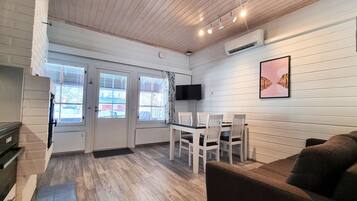 A room with a wooden ceiling, white walls, a dining table with chairs, a sofa, and a TV mounted on the wall.
