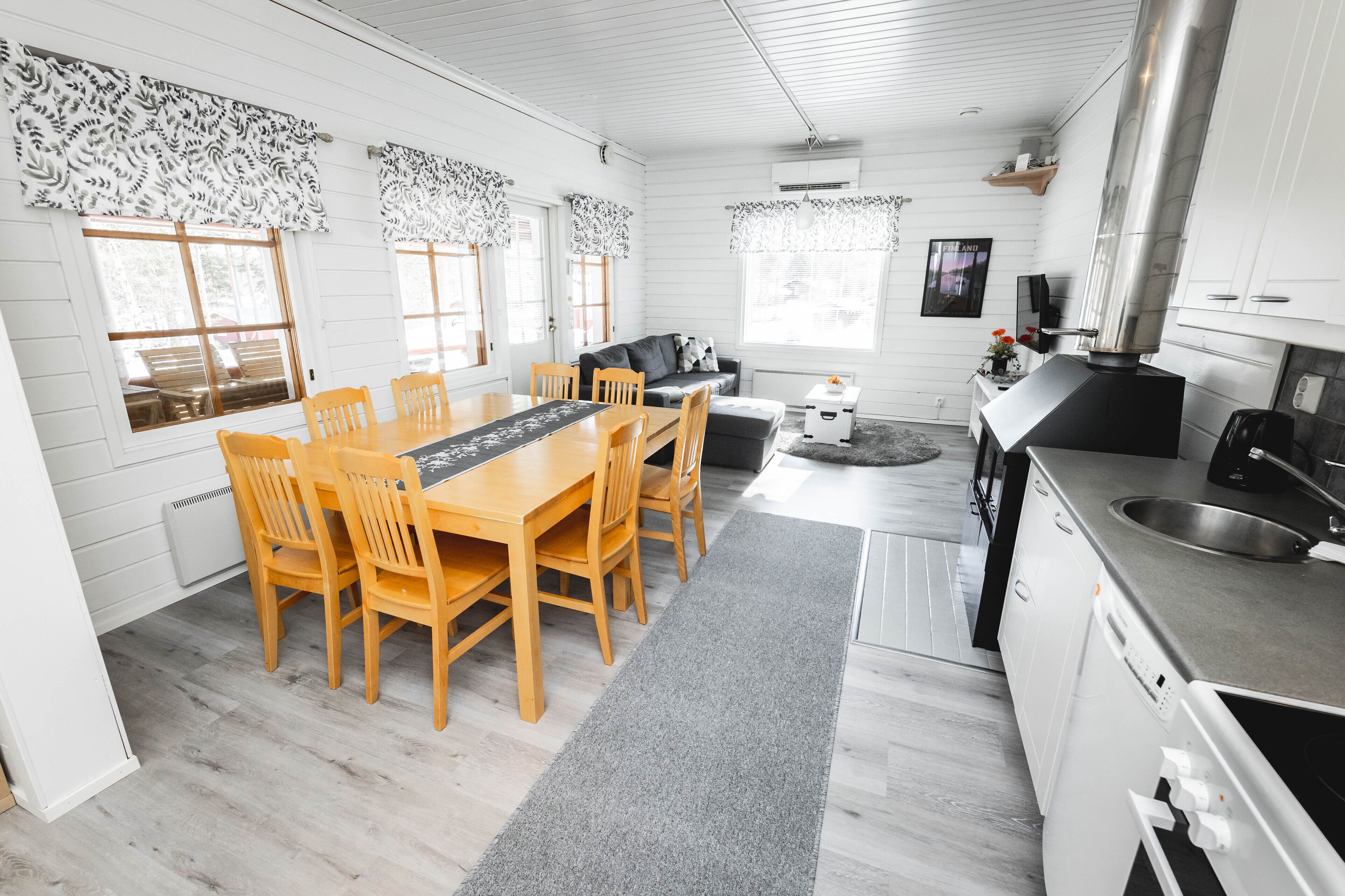 A modern kitchen with white cabinetry, a stainless steel range hood, and a dining area with wooden chairs and a table.