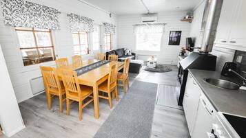 A modern kitchen with white cabinetry, a stainless steel range hood, and a dining area with wooden chairs and a table.