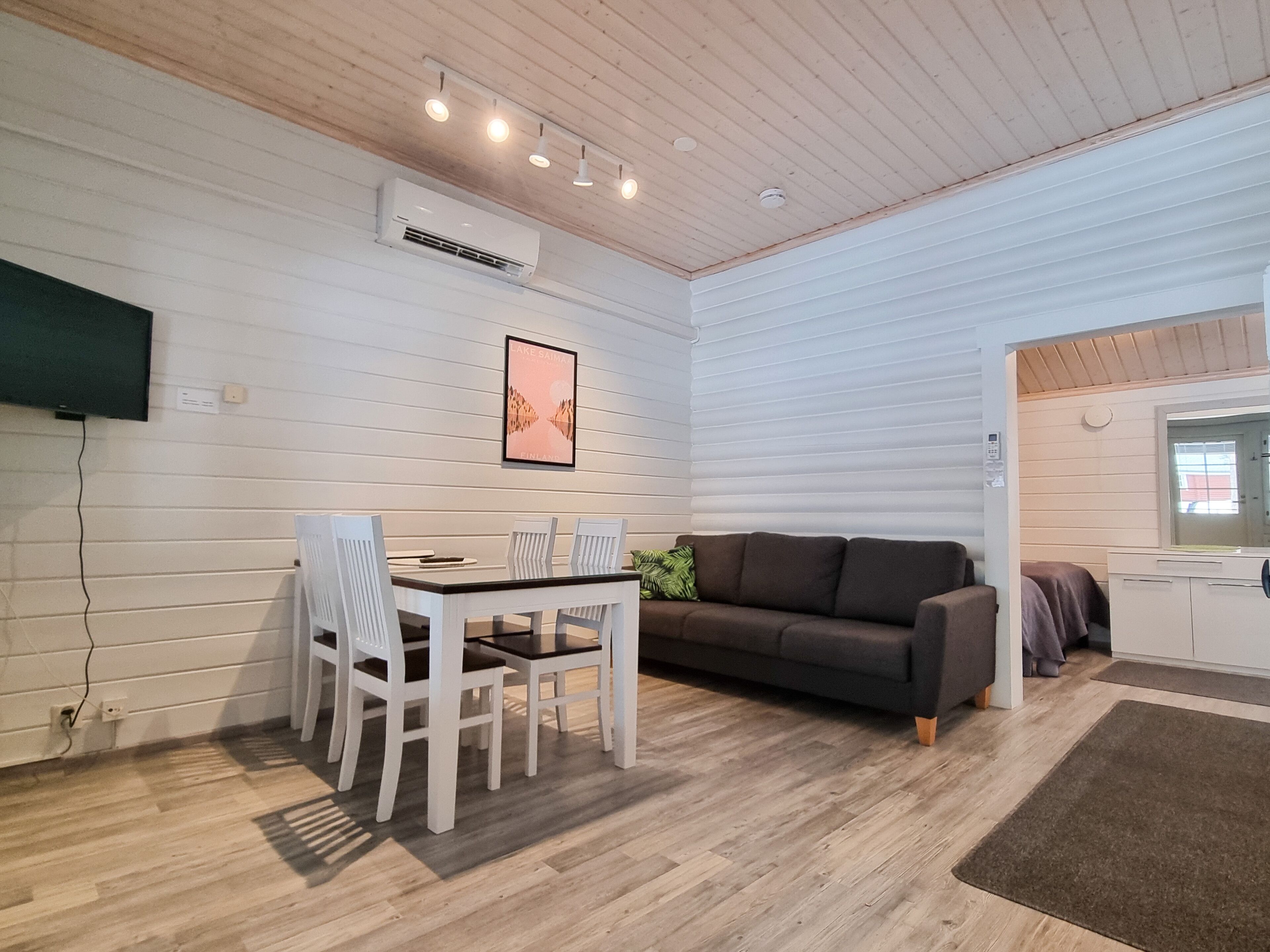 Een moderne woonkamer met een houten plafond, witte muren, een eettafel met stoelen, een bank en een groot raam.