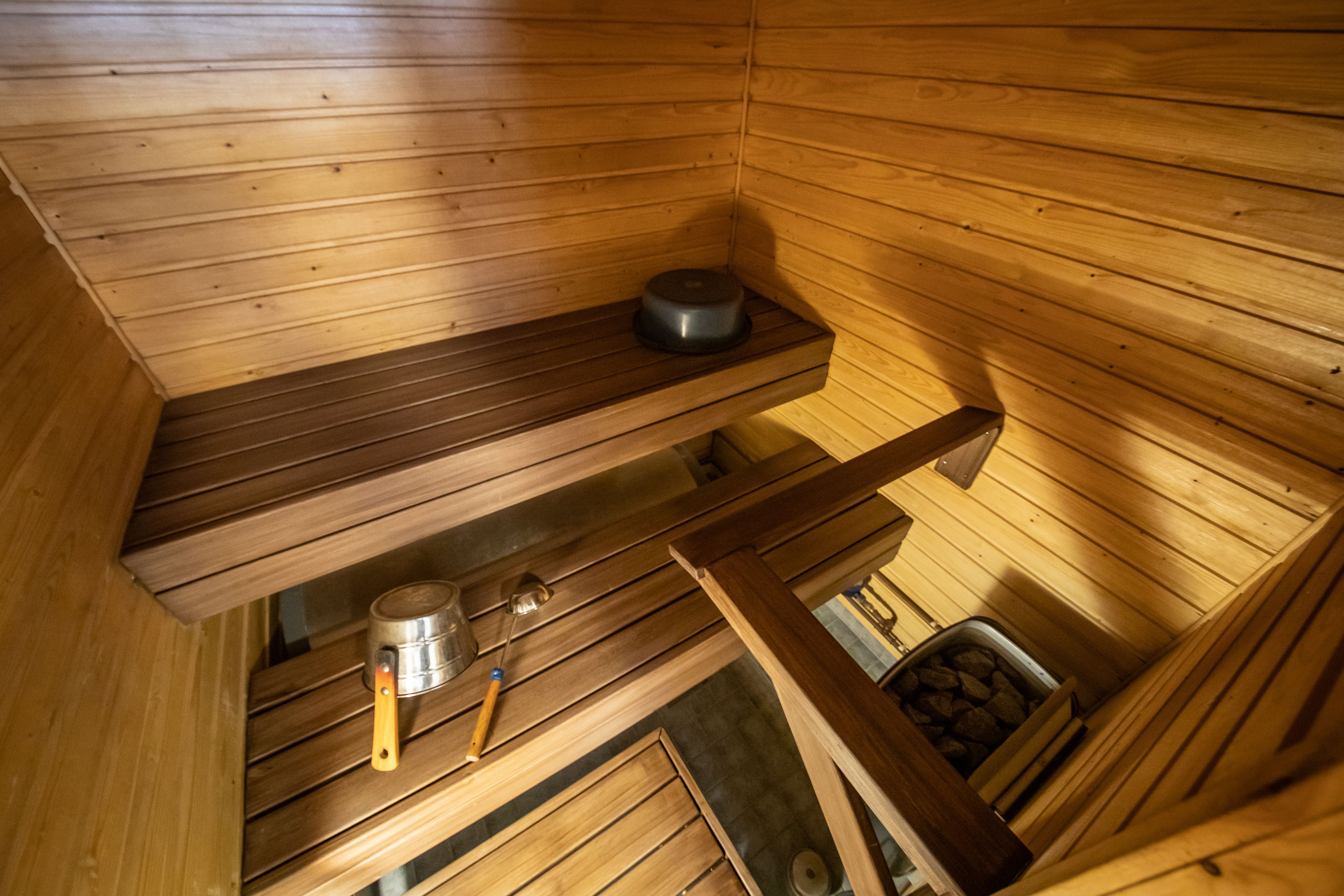 A sauna with wooden walls and benches, a metal container, and a wooden door.