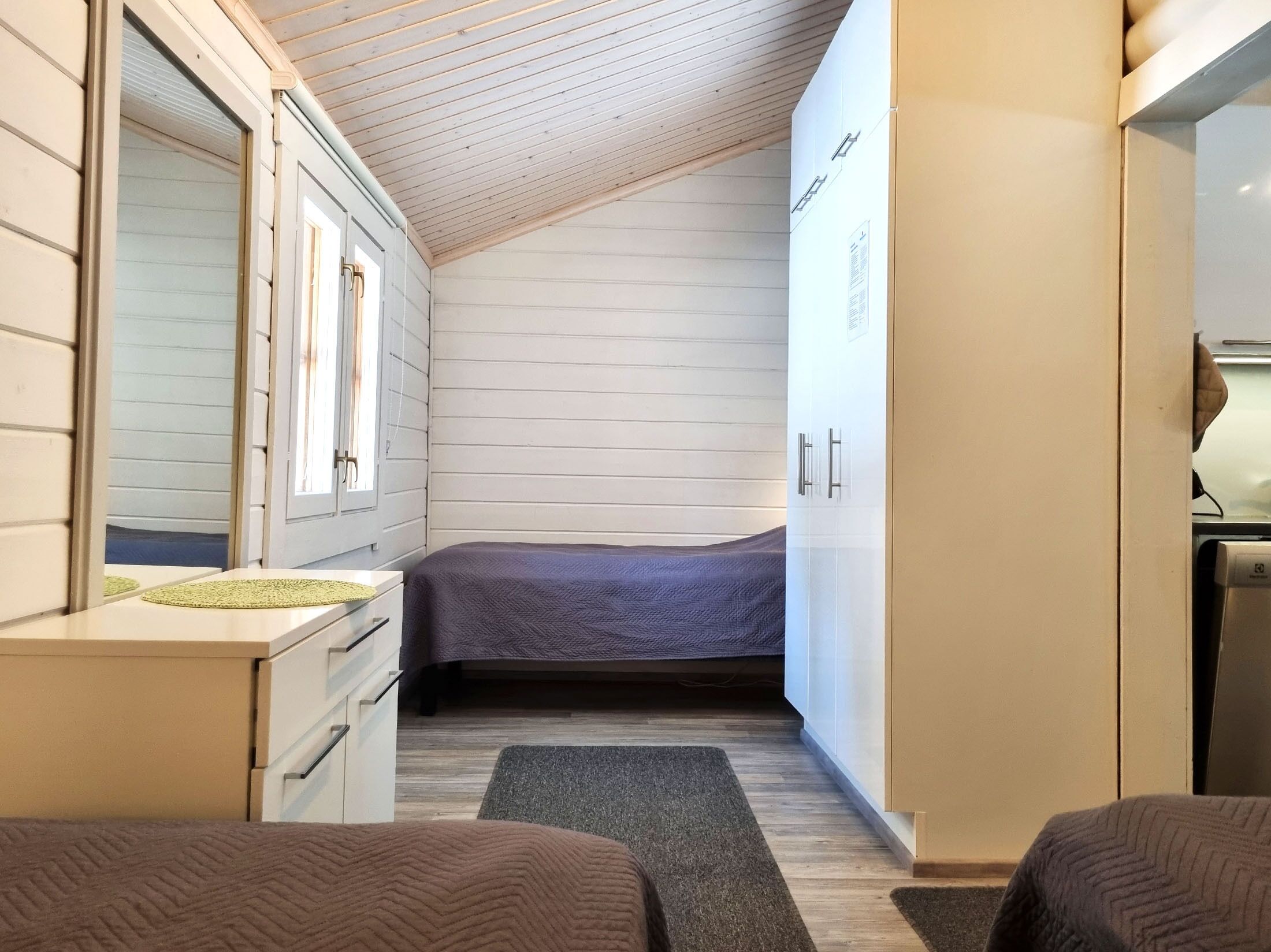 Quarto compacto com cama, uma pequena escrivaninha e um guarda-roupa.