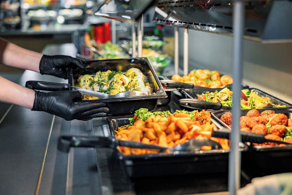 A buffet with various dishes including a tray of chicken and vegetables, a tray of meatballs, and a tray of fries.