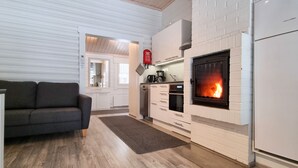 A modern kitchen with a built-in fireplace, wooden flooring, and a grey sofa. - Holiday Resort Harjun Portti (Savonlinna)