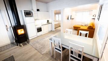 A compact, modern kitchen with a wood-burning stove, white cabinetry, and a dining area with a glass table and chairs.
