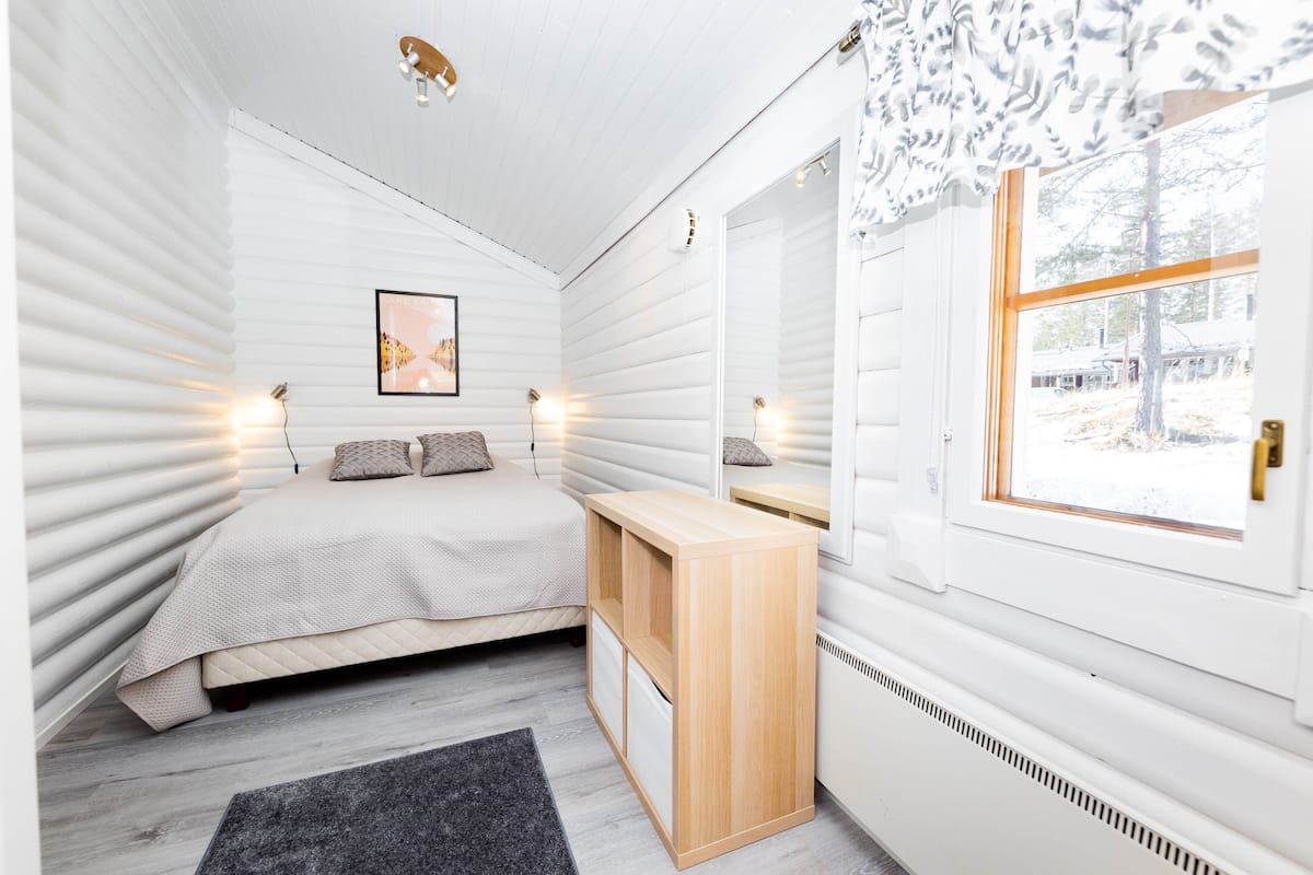 A bedroom with a bed, bedside tables, a mirror, and a window with a view of the outside.