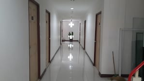 A long, narrow hallway with doors on both sides, a central light fixture, and a potted plant at the end. - P.F Mansion (Koh Samui)