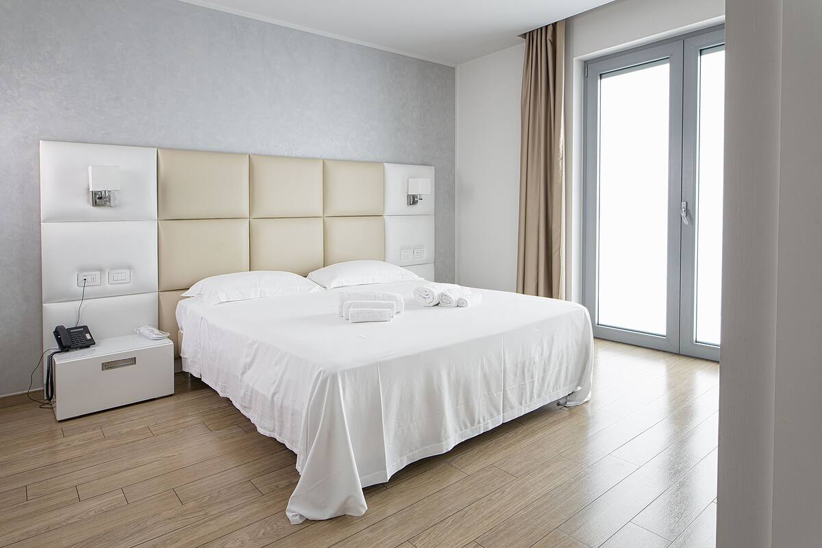 A modern hotel room with a large bed, bedside tables, and a view of the outdoors.