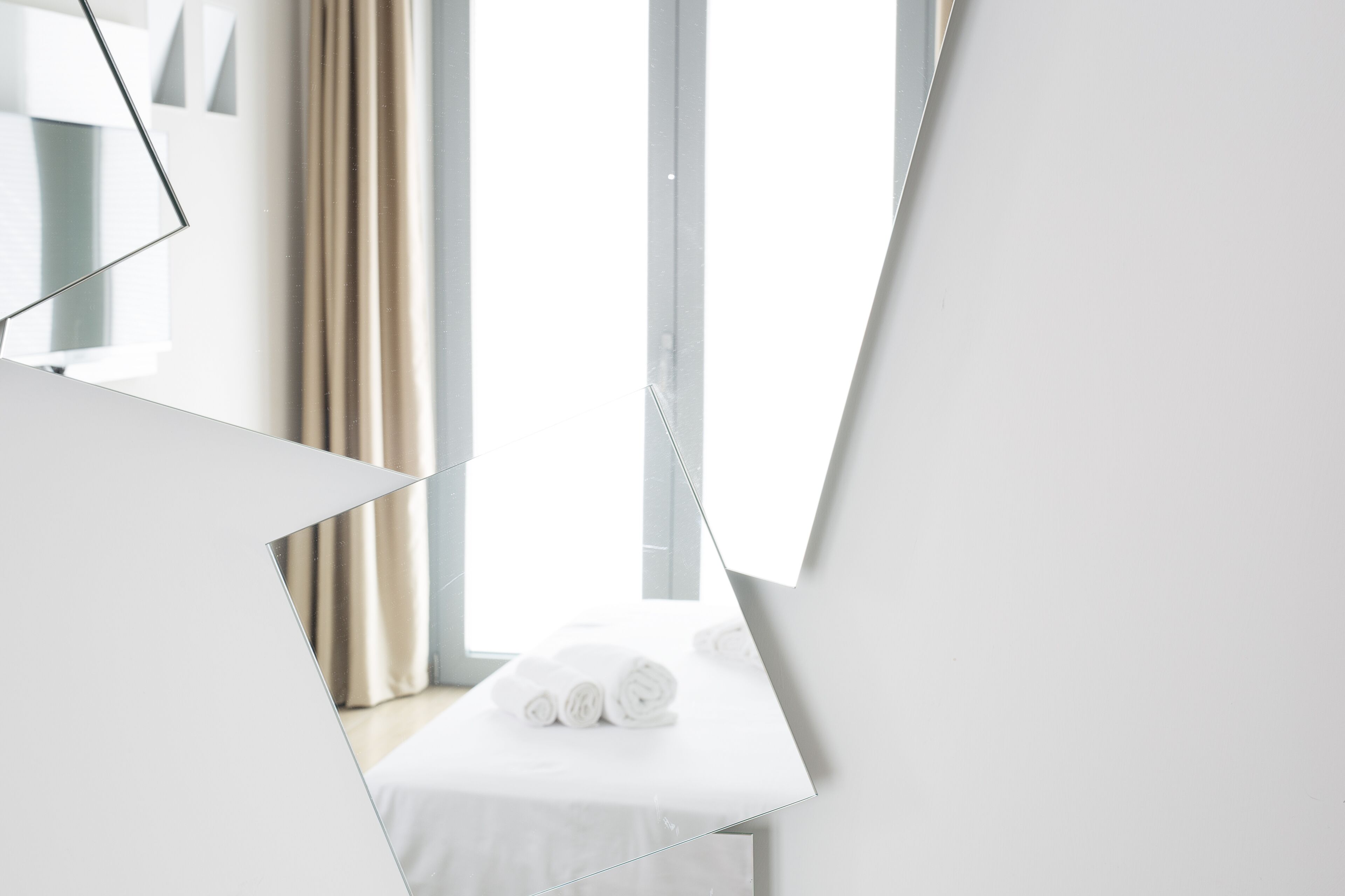 A modern hotel room with a neatly made bed, a large window with curtains, and a minimalist design.