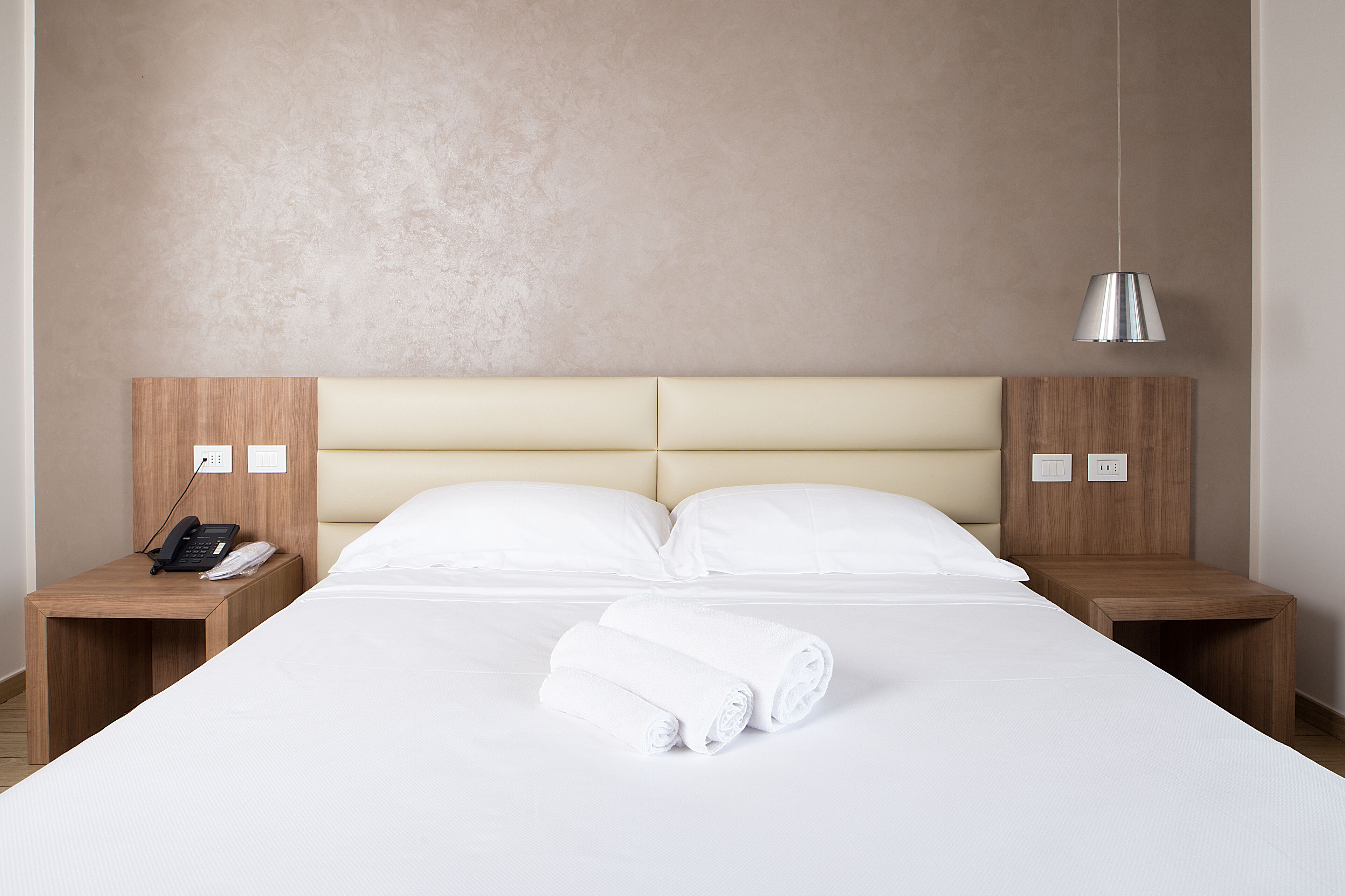 Una habitación de hotel con una cama grande, dos mesitas de noche, una lámpara y un teléfono sobre una de ellas.