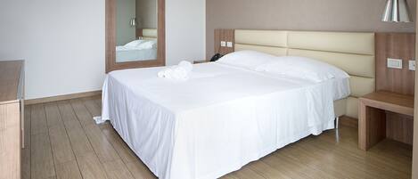 Una habitación de hotel con una cama grande, una mesita de noche, un espejo y suelo de madera.
