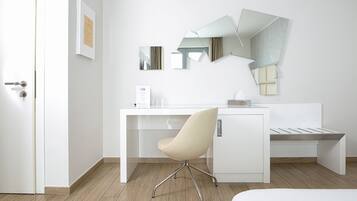 A modern hotel room with a white desk, a chair, and a bed.