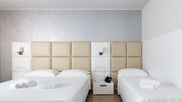 A hotel room with two beds, a bedside table with a phone and a lamp, and a wall-mounted light fixture.