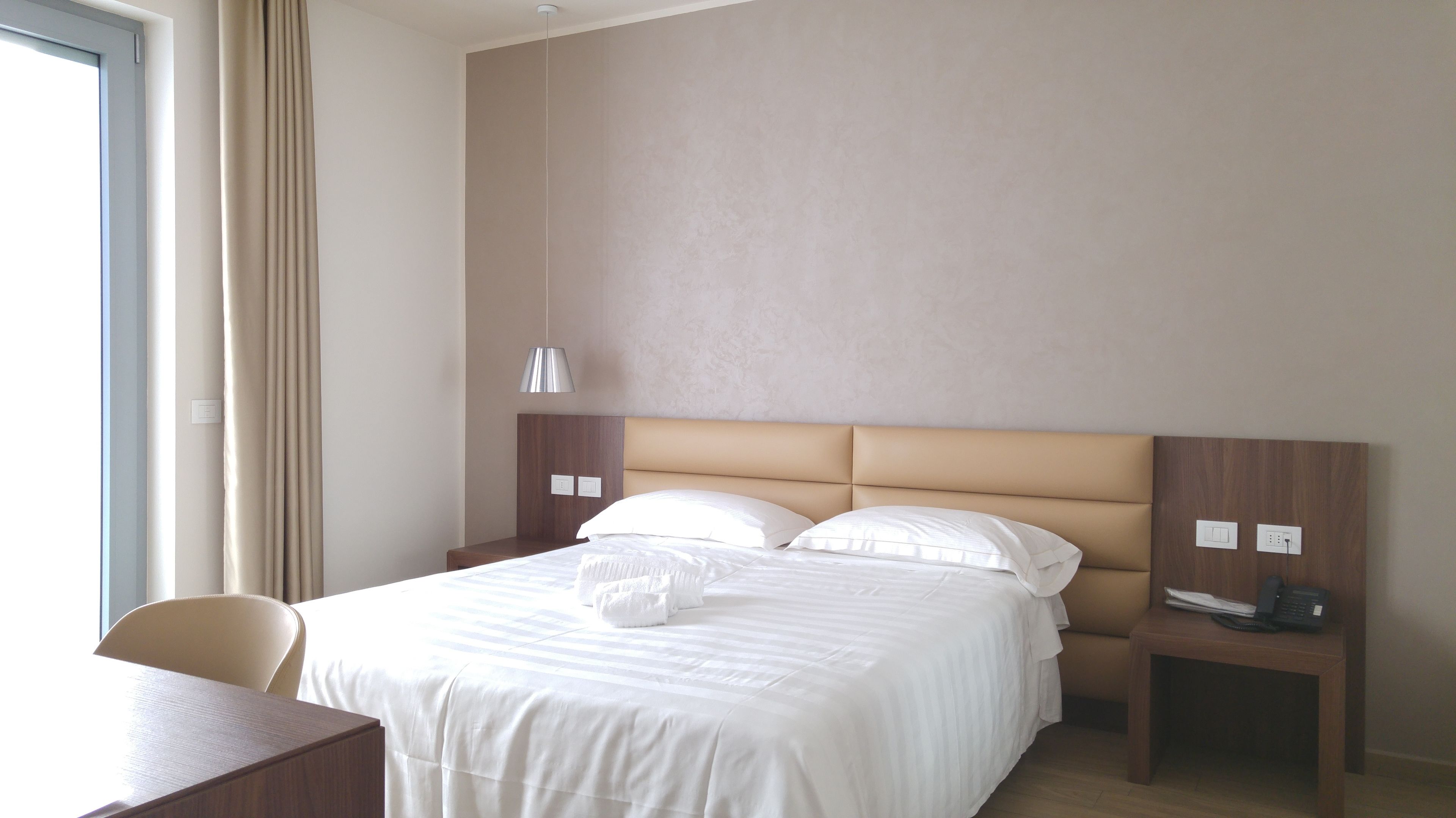Ein Hotelzimmer mit einem Bett, einem Schreibtisch, einem Stuhl, einer Lampe und einem Telefon.