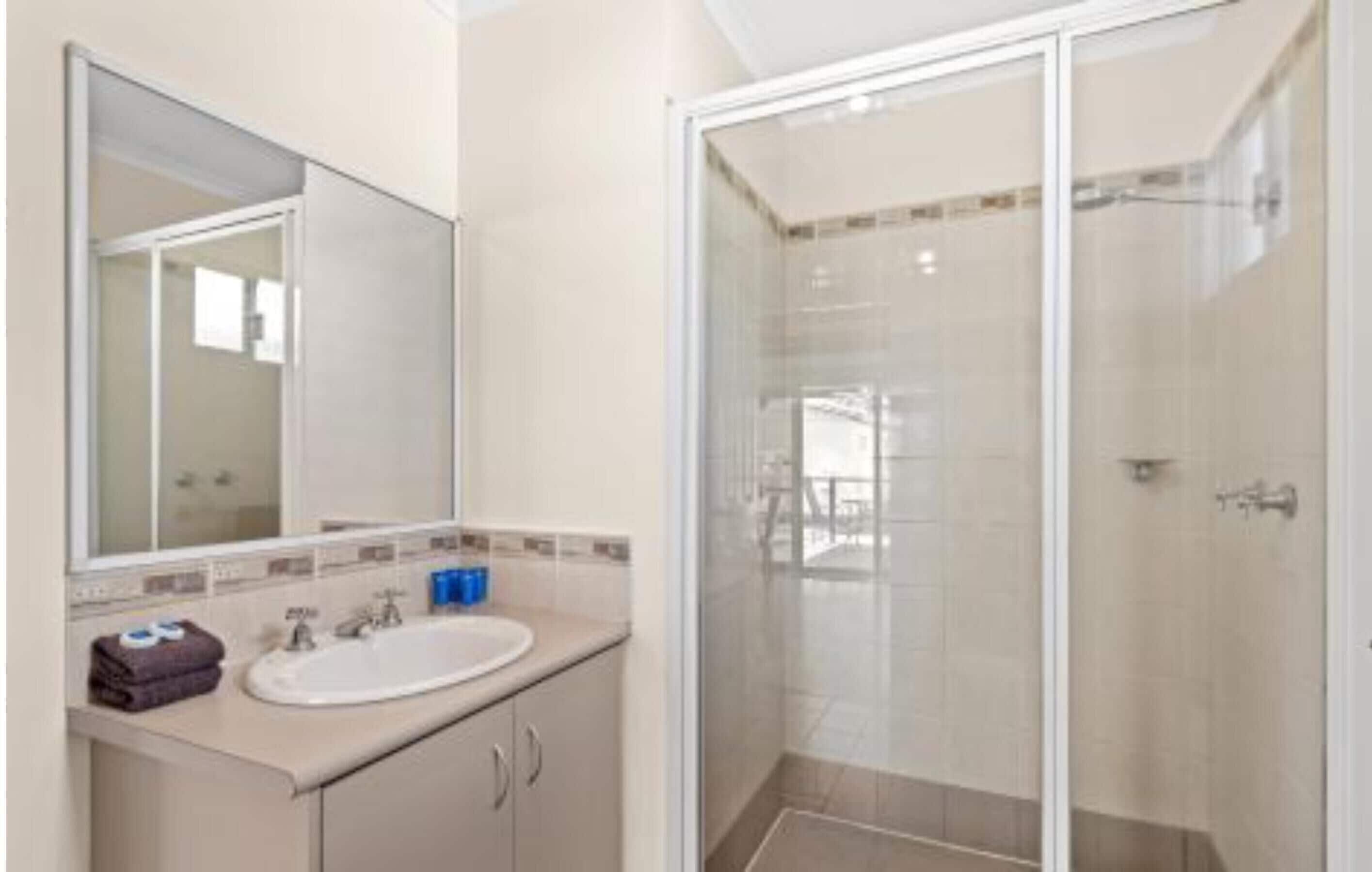 A bathroom with a sink, mirror, and shower enclosure.