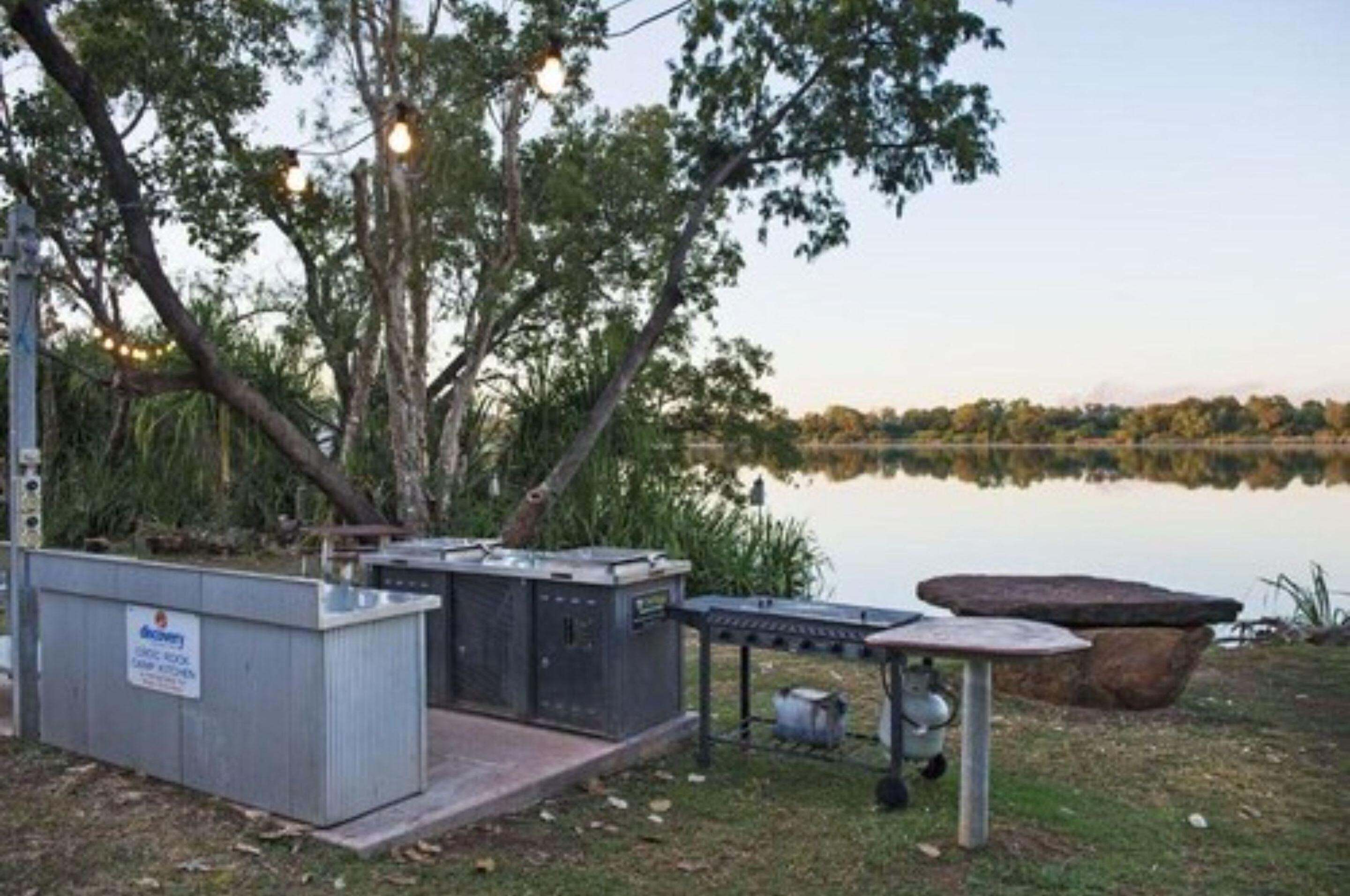 A lakeside outdoor area with electrical boxes, a table, and a fire pit.