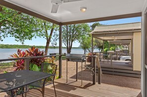 Een overdekt terras buiten, met een barbecue, zitplaatsen en uitzicht op het meer.