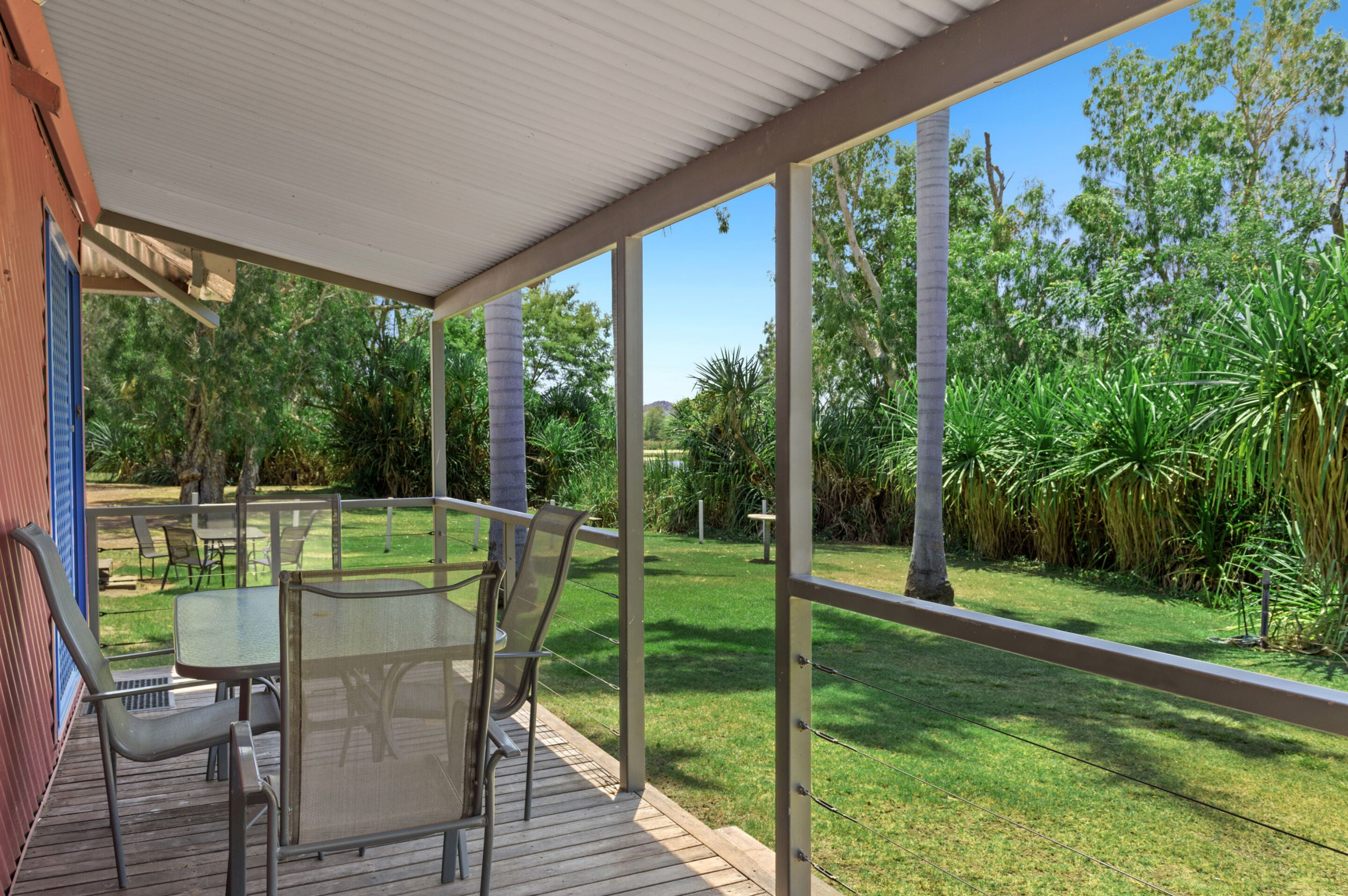 A covered outdoor area with a table and chairs, surrounded by lush greenery and a clear view of the landscape.
