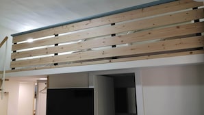 Une pièce dotée d’un plafond à lattes, d’un téléviseur à écran plat fixé au mur et d’une porte donnant accès à une salle de bain.