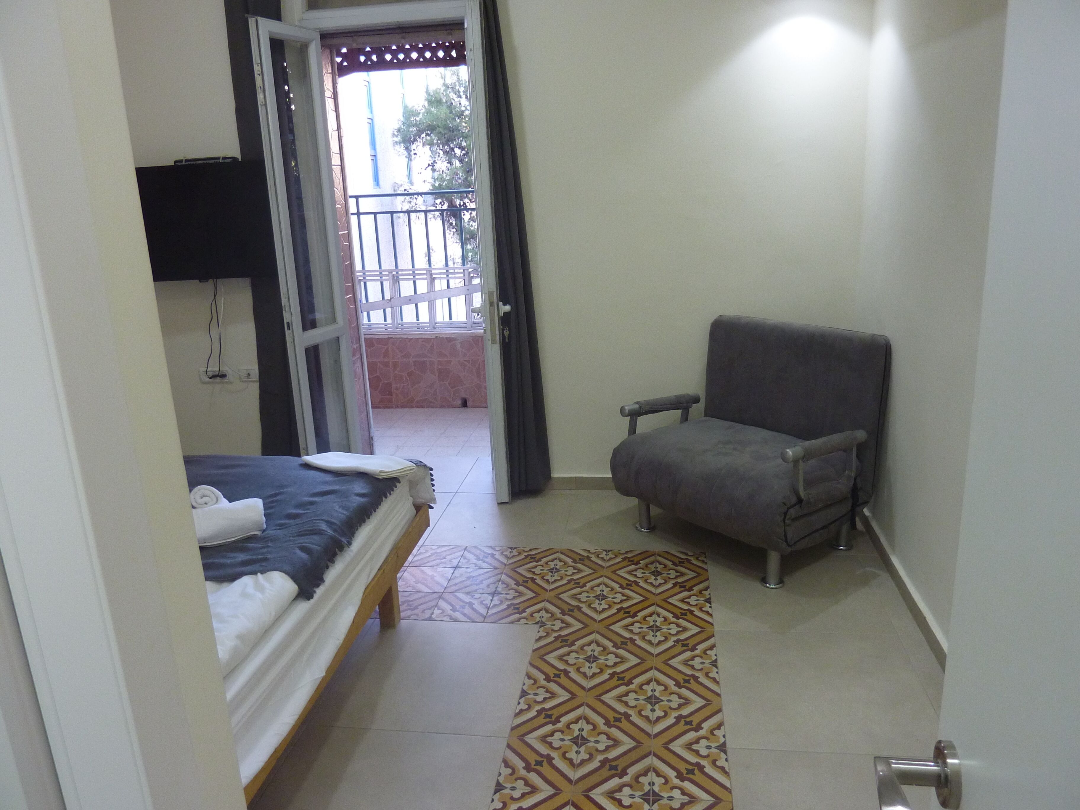 Ein Hotelzimmer mit einem Bett, einem grauen Sessel, einem gemusterten Teppich und Blick auf den Balkon.