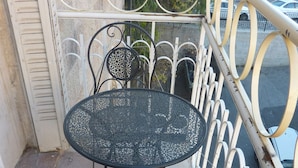 Un balcon doté d’une table ronde en métal et de deux chaises, le tout entouré d’une rambarde en métal blanc.
