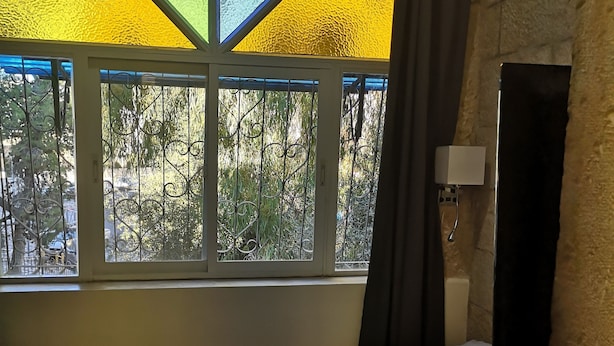 Une chambre avec un lit, une fenêtre ornée de vitraux et une vue sur la verdure environnante.