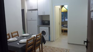 Une cuisine compacte équipée d’un réfrigérateur, d’un four à micro-ondes et d’un lave-linge. Une table à manger, avec des chaises et de l’assiette, est installée dans la pièce.