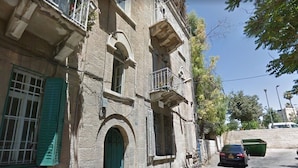 Un bâtiment historique à la façade en pierre, doté de volets verts et d’un petit balcon.