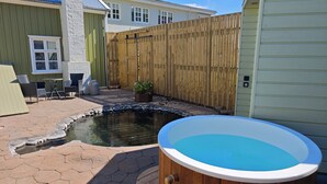 Un jardin avec un jacuzzi, un petit étang, du mobilier de jardin et une clôture en bois.