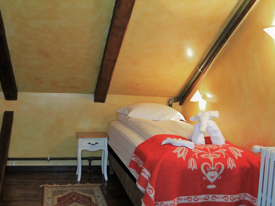 A bedroom with a bed, a nightstand, a radiator, and a wooden floor.