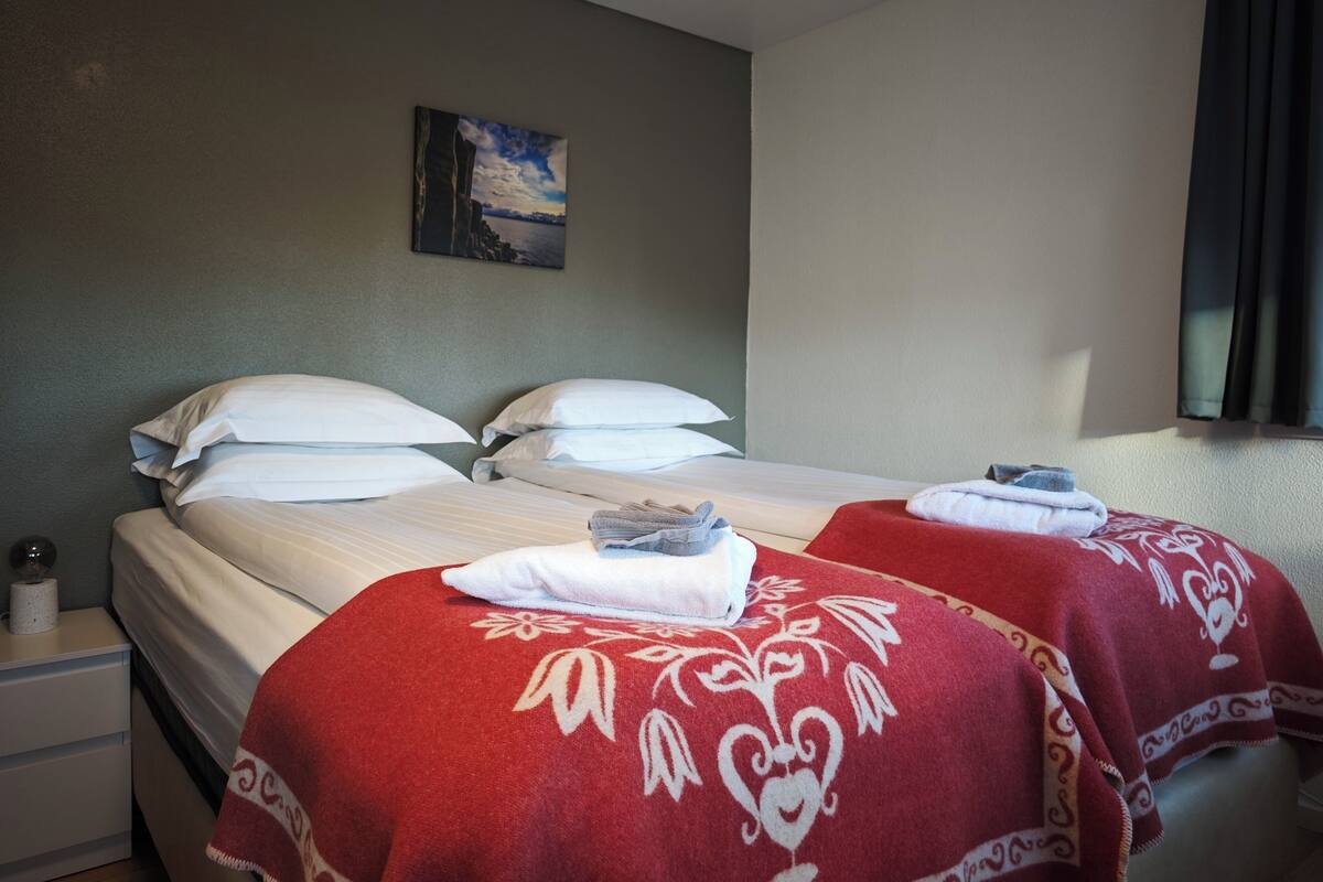 A hotel room with two beds, a painting on the wall, and a window with curtains.