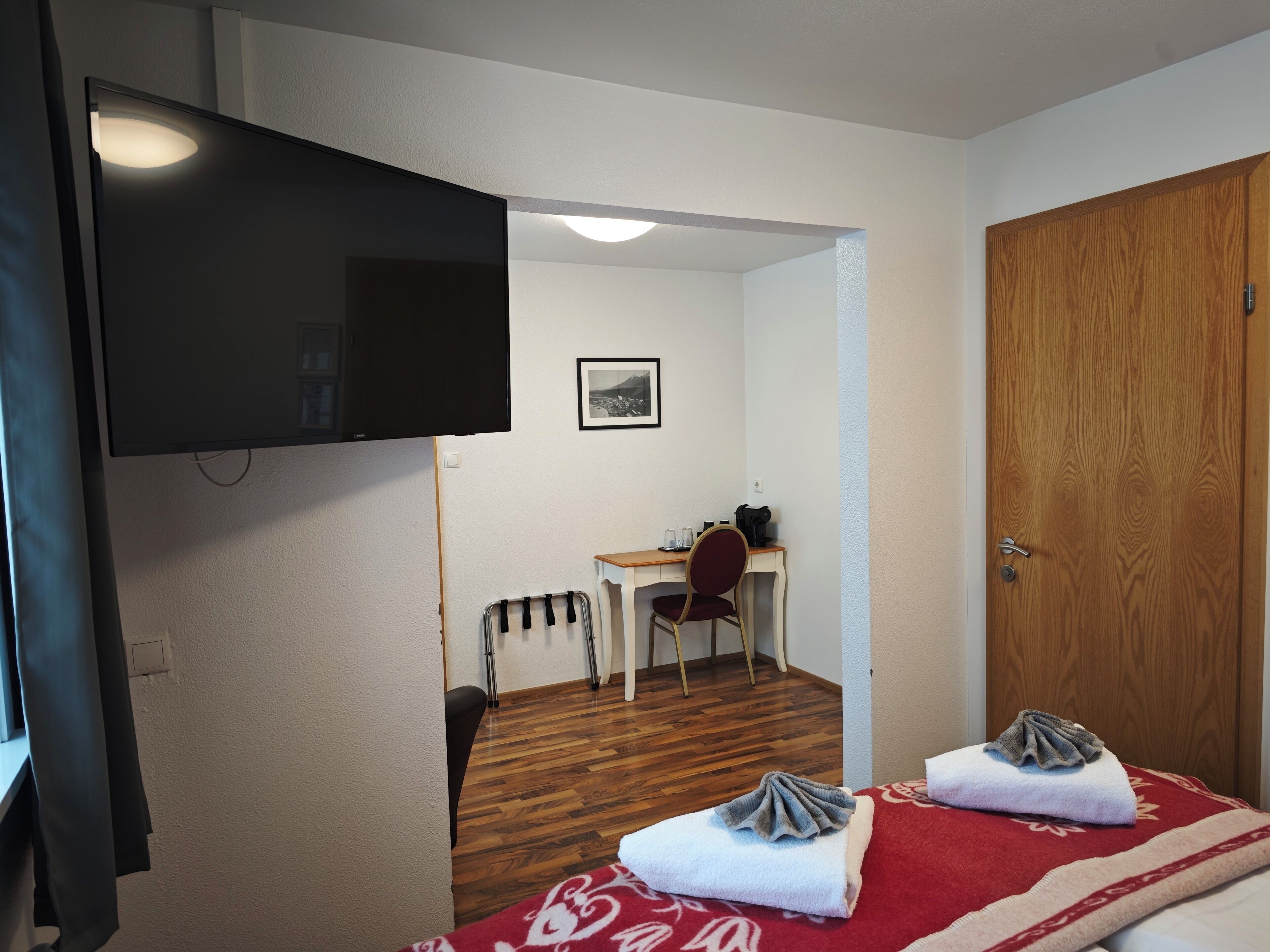 Une chambre d’hôtel avec un lit, un bureau, une chaise, une télévision et une porte en bois.
