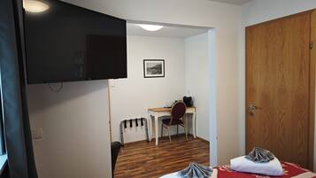A hotel room with a bed, a desk, a chair, a television, and a wooden door.
