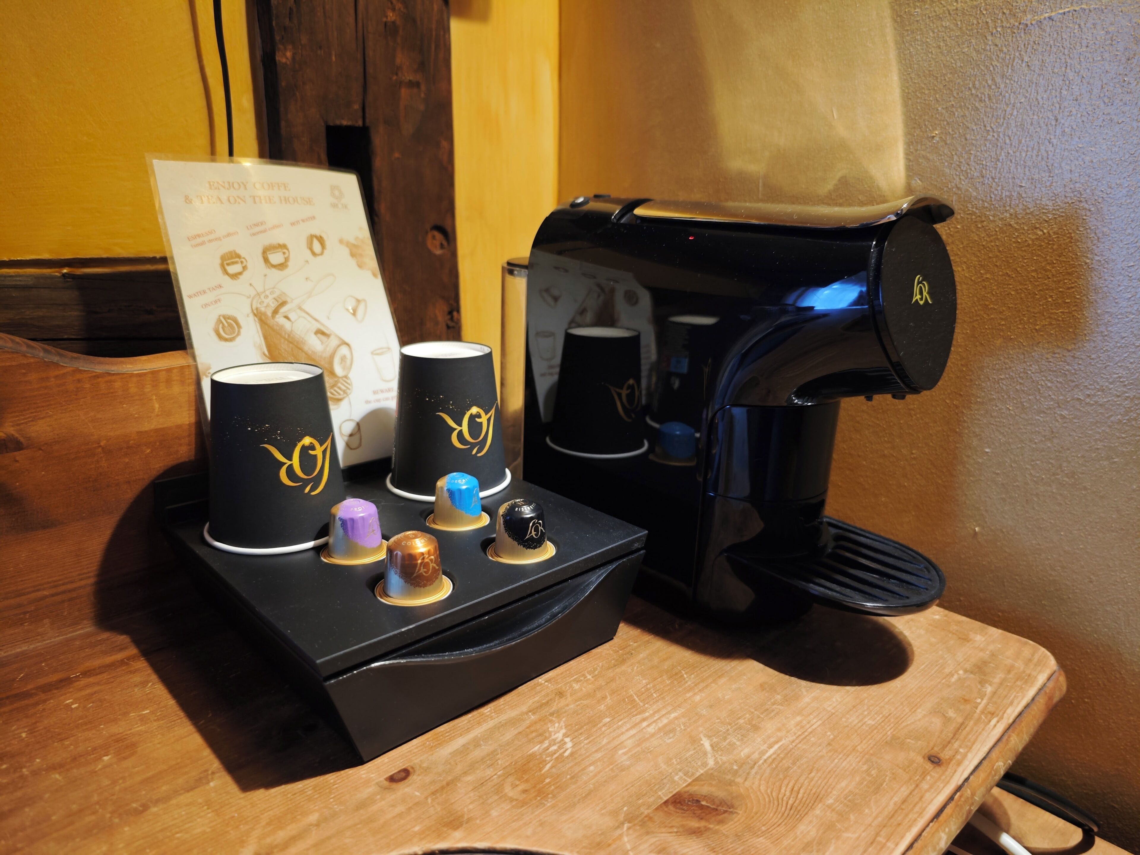 A coffee machine with four cups on a wooden table, a menu, and a wooden door in the background.