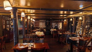 L’intérieur d’un restaurant avec des tables et des chaises en bois, des luminaires suspendus et un mur en pierre.