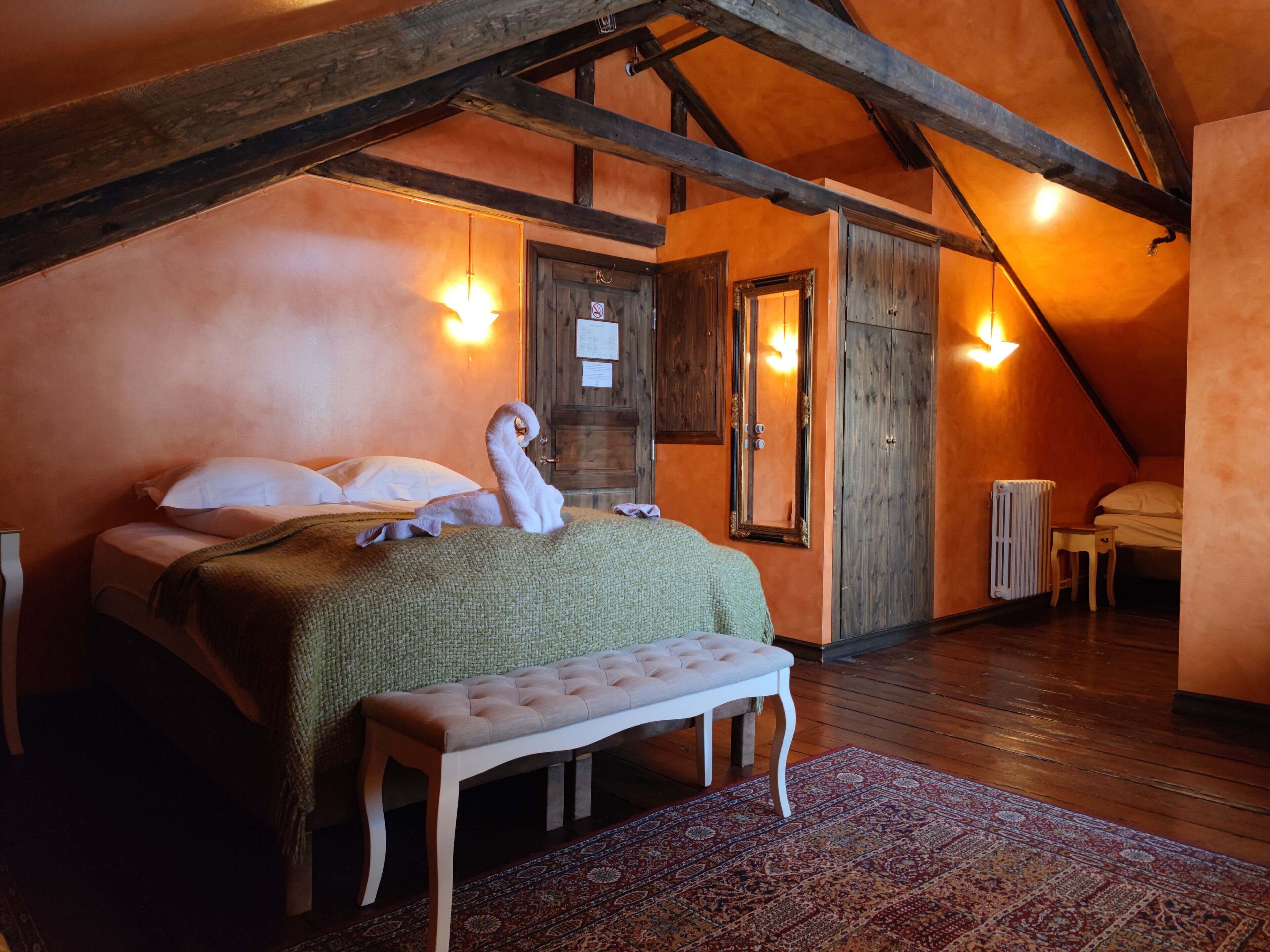 A bedroom with a bed, bench, wooden beams, and a radiator.