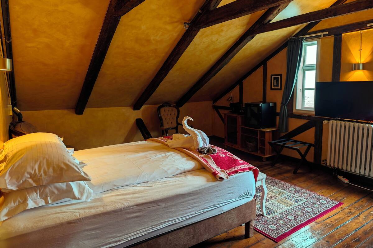 A bedroom with a bed, a chair, a desk, a television, and a window.