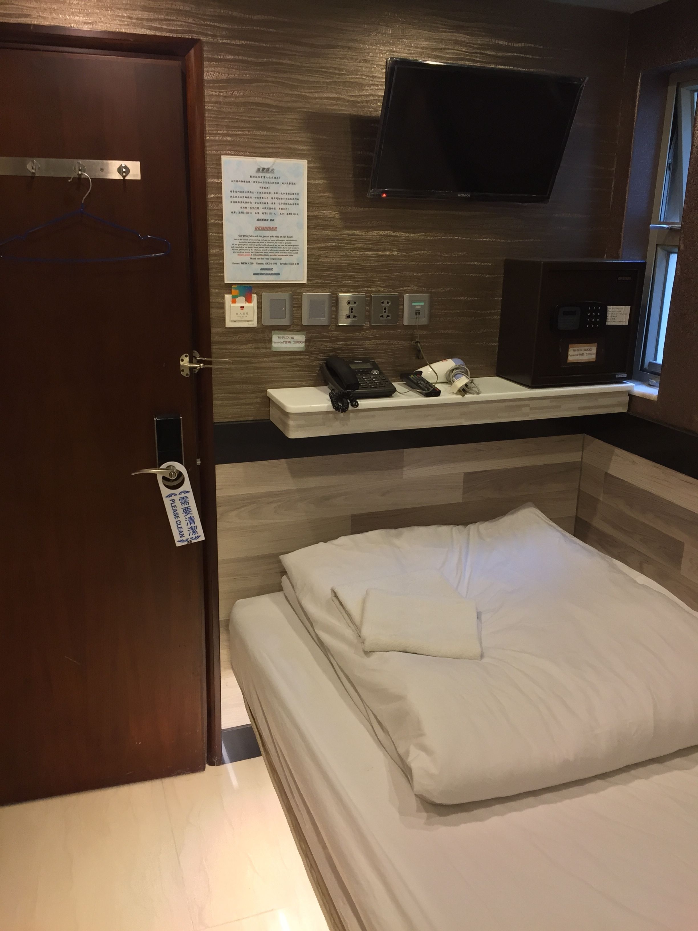A hotel room with a bed, a desk with a telephone, a microwave, and a television mounted on the wall.