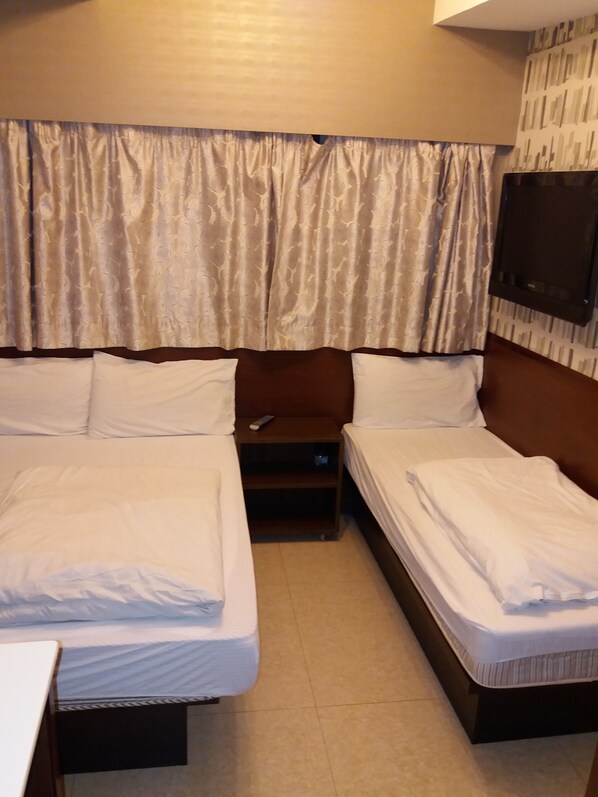 Habitación de hotel con dos camas individuales, una mesita, una mesita de noche y un televisor montado en la pared.