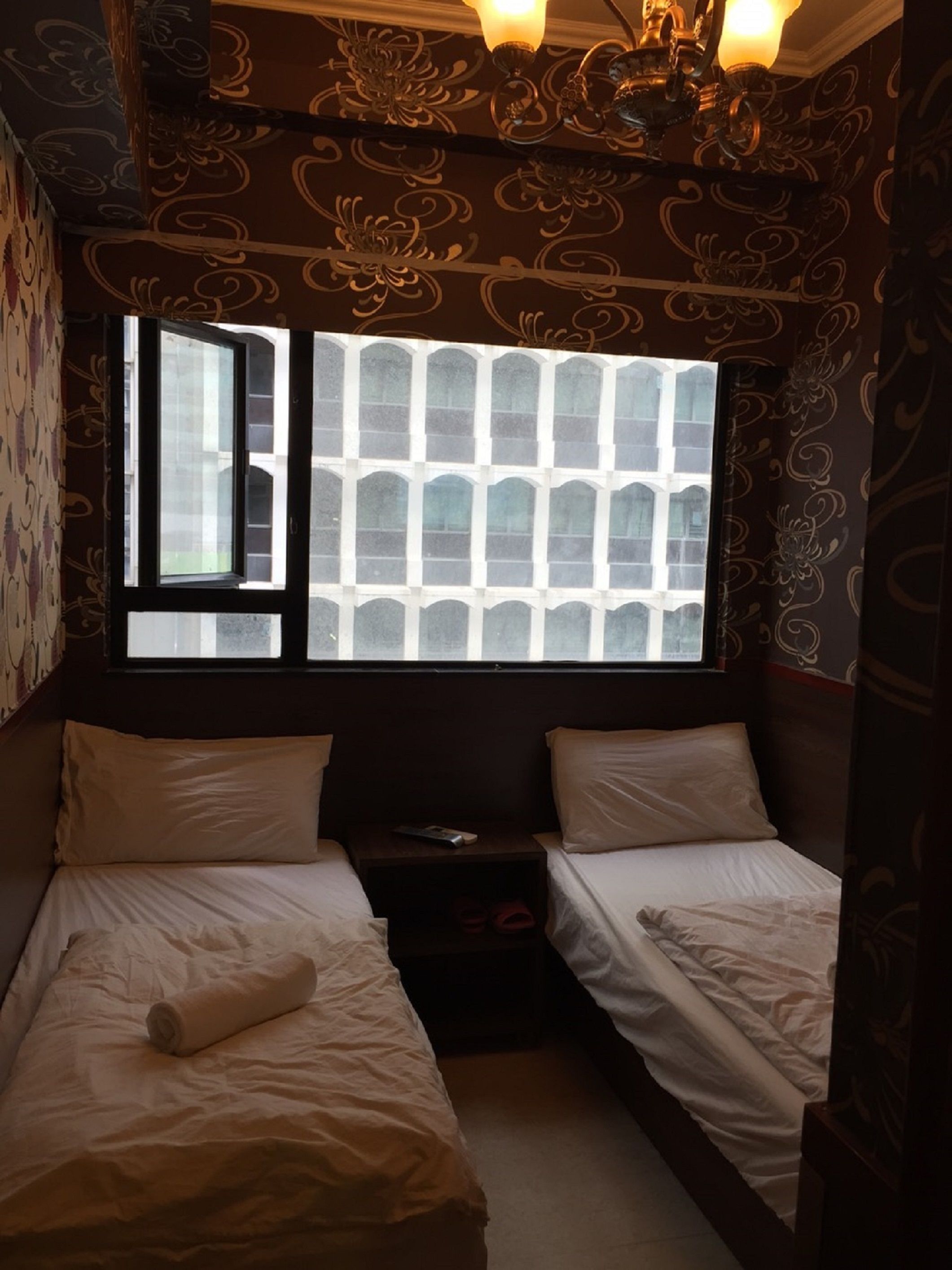 Una habitación con dos camas individuales, una mesita y un ventanal con vistas a un edificio.