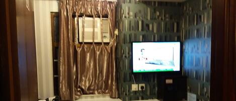 A hotel room with a bed, a TV, a vanity with a mirror, and a window with curtains.
