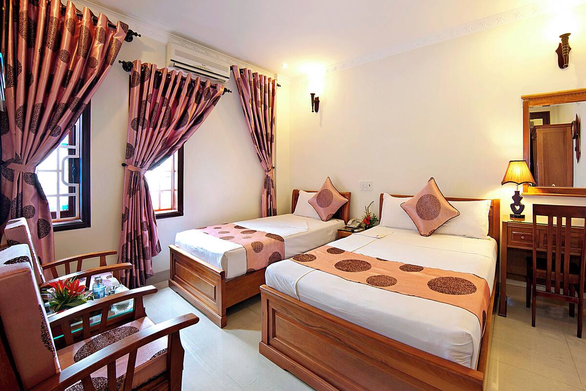 A hotel room with two beds, a desk, a chair, a lamp, and a mirror.