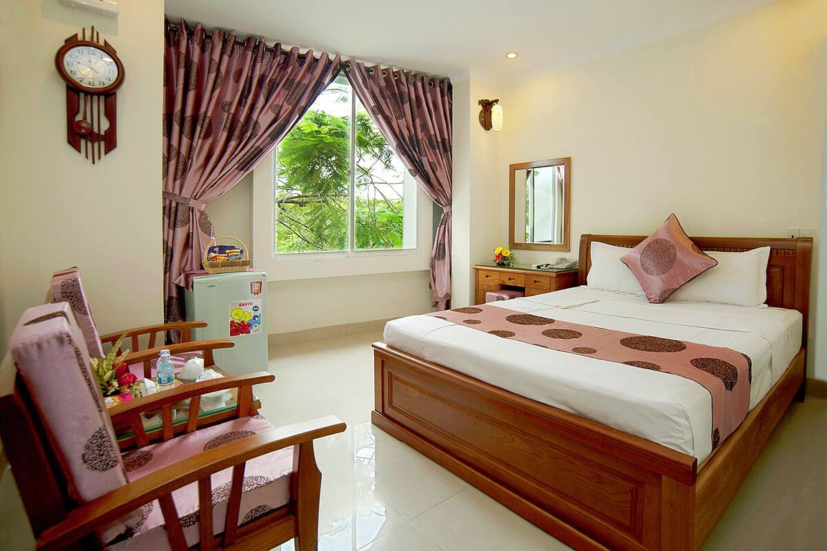 A bedroom with a bed, a desk, a chair, a clock, and a window with curtains.