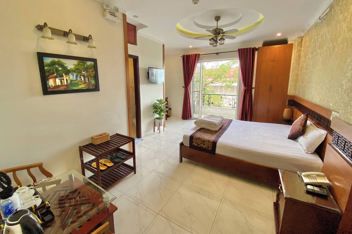 A hotel room with a bed, a desk with a telephone, a television, and a painting on the wall.