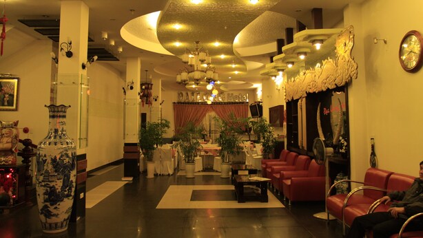 A hotel lobby with a central seating area, a reception desk, and a large mirror on the right. - Dai Long Hotel (Da Nang)