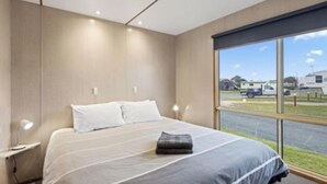 Une chambre d’hôtel moderne, dotée d’un grand lit, d’une table de chevet et d’une fenêtre donnant sur un parking.