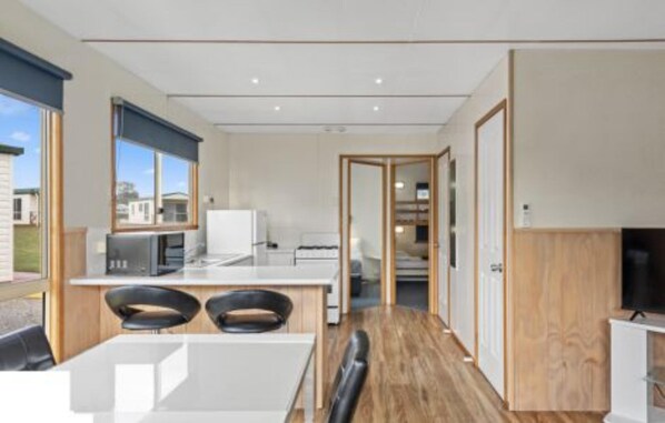 A modern kitchen with a microwave, stove, and dining area with two chairs. - Discovery Parks - Devonport (East Devonport)