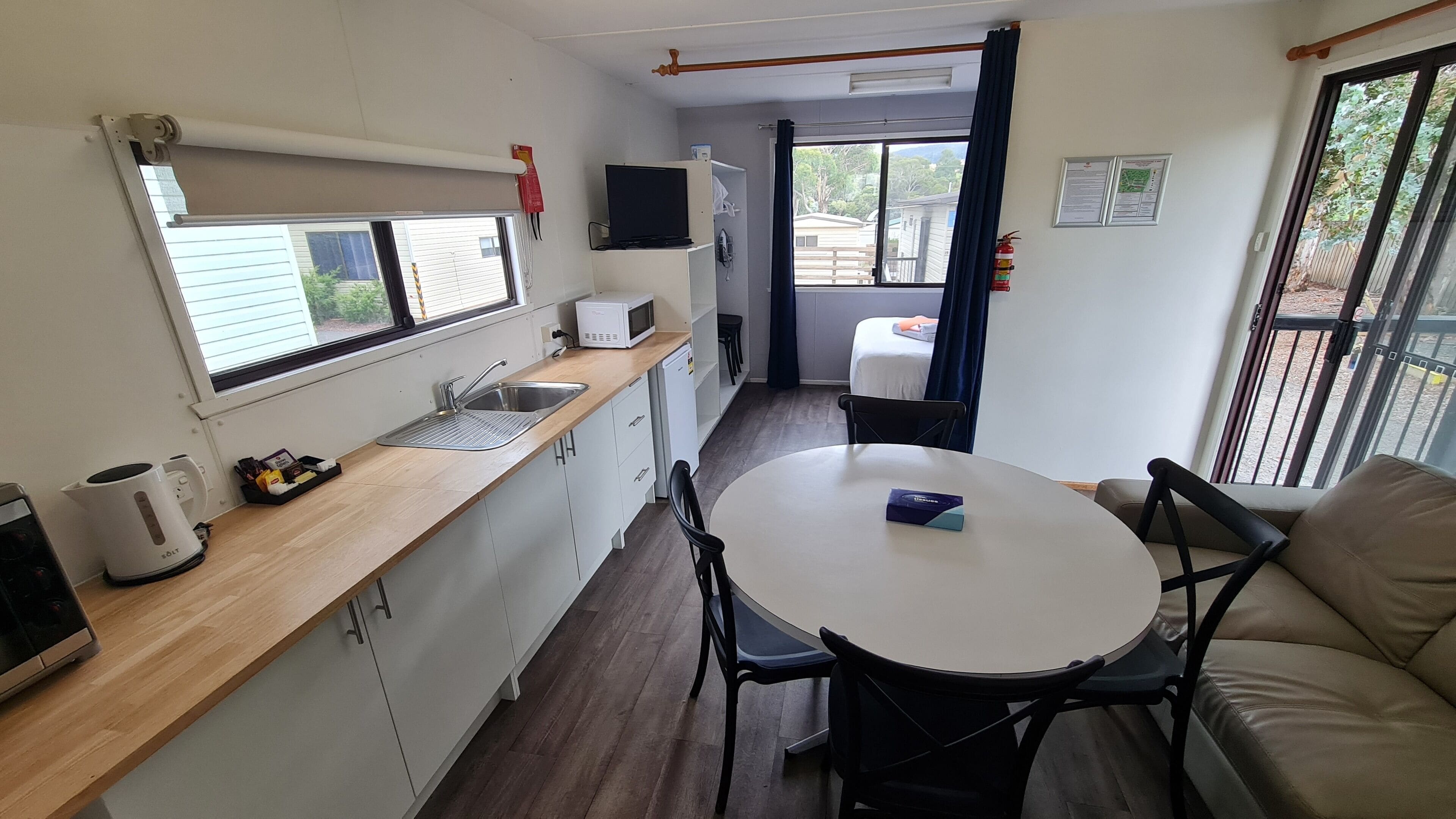 Une petite cuisine équipée avec un four à micro-ondes, une bouilloire et un évier. On y trouve également une petite table à manger avec des chaises, et une fenêtre donnant sur l’extérieur.