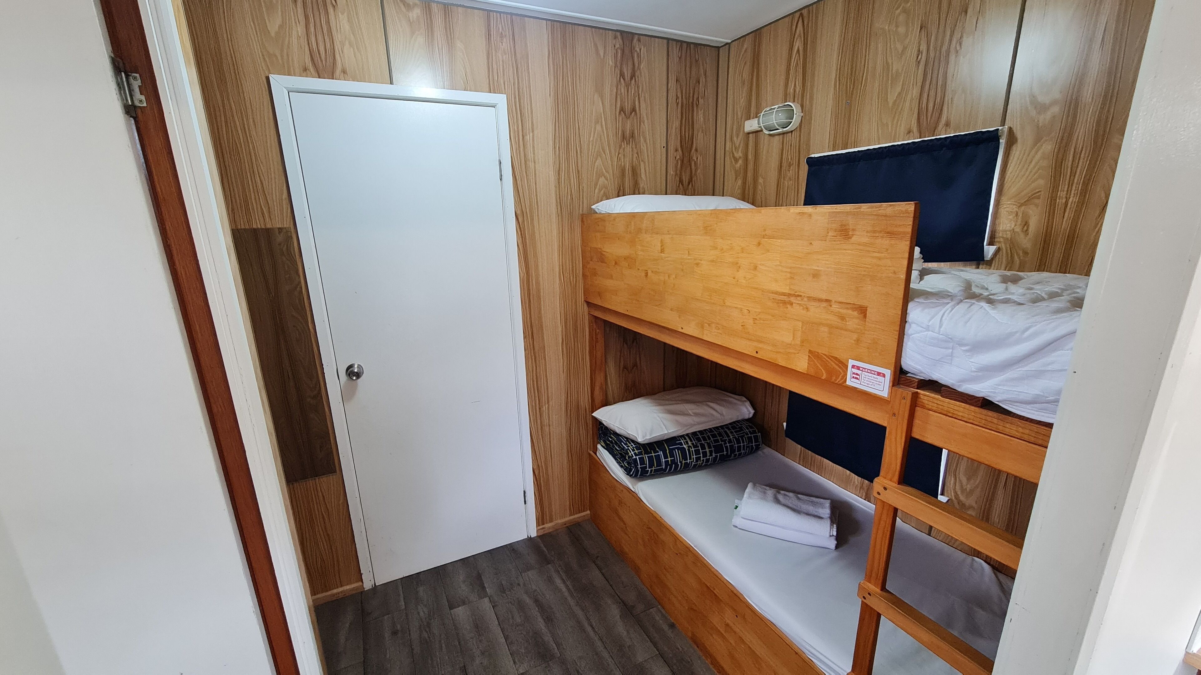 Quarto pequeno com uma cama beliche, um guarda-roupa e uma prateleira com toalhas dobradas.